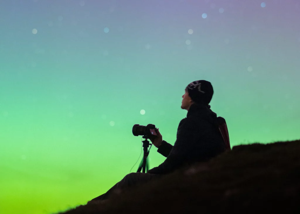 Photographe au trépied sous une aurore boréale verte