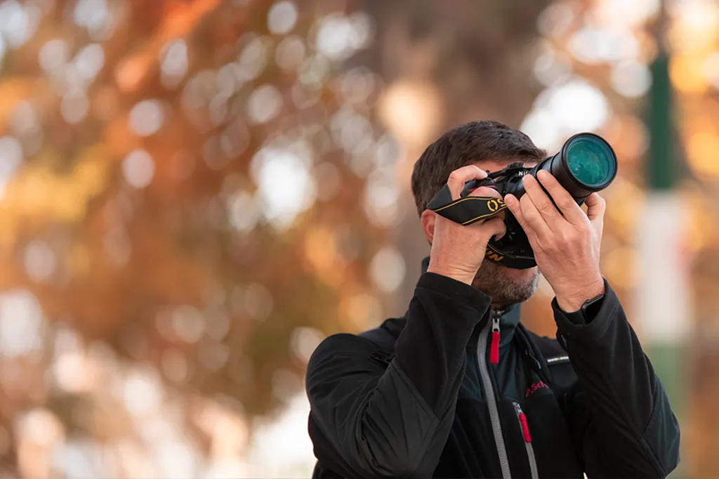 Photographe tenant un téléobjectif, arrière-plan automnal