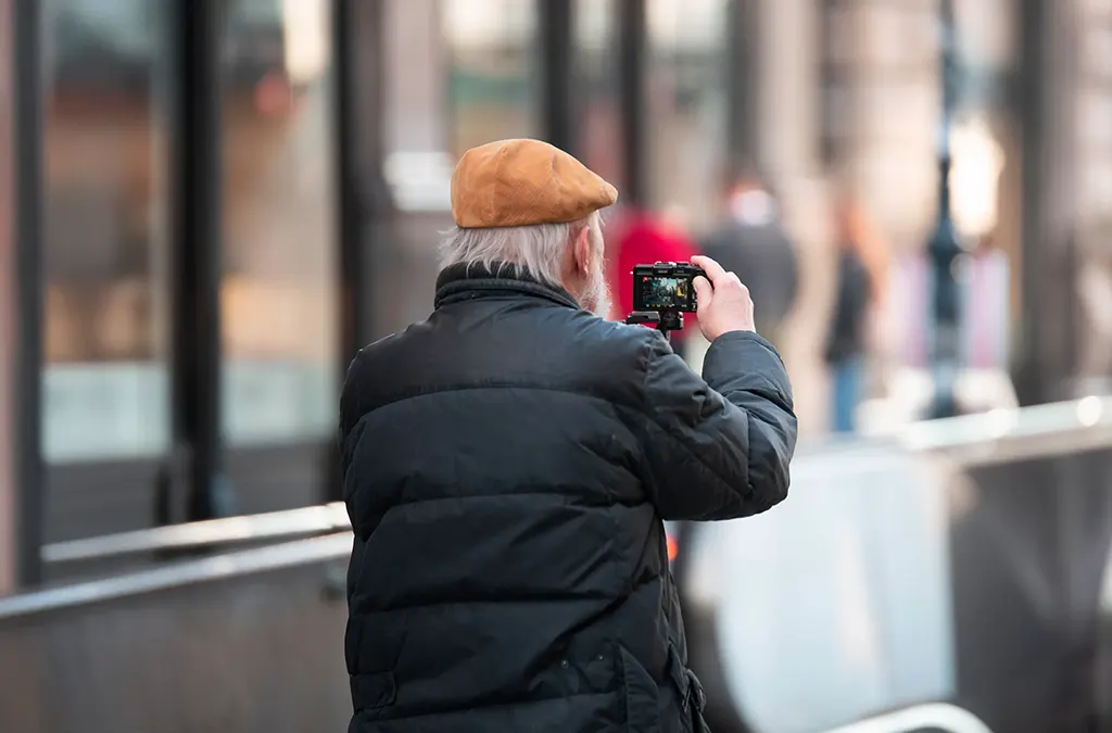 Homme photographiant de dos, scène urbaine floutée en arrière-plan